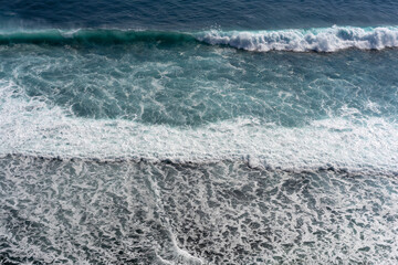 Abstract aerial view of powerful ocean waves. Layers of deep blue water, turquoise surf, and white foam create a stunning natural texture.