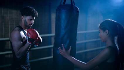 Indian young adult gen z angry fit boxer man guy wear gloves do hand fist boxing punch beat hit on bag indoor dark class room place modern sports smart male boy learn self defense martial art skill