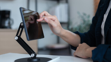 Close-up hand using a tablet on a stand with touchscreen technology. Concept of digital device, smart technology, online communication, remote work, mobile office, and modern lifestyle.