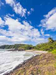 Tropical Beach and Rocky Shoreline under Bright Sun and Blue Sky
