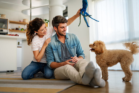 Happy couple playing with dog, having fun on floor at home. Married couple with cute pet - Powered by Adobe