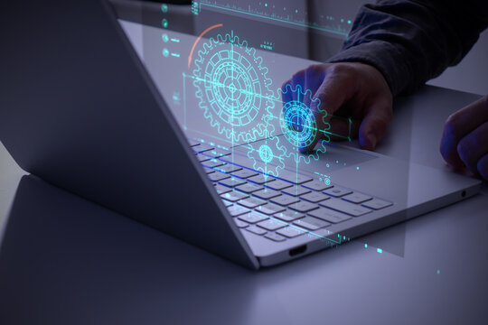 Person using a laptop with a glowing gears icon. Concept of business process workflow optimization and automation, digital transformation, robotic process automation and flowing process management.