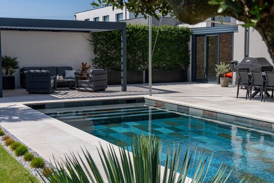 Salon de jardin moderne avec pergola install&eacute; devant une piscine, cr&eacute;ant un espace de d&eacute;tente ext&eacute;rieur &eacute;l&eacute;gant.