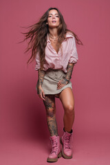 Confident woman poses in pink background wearing stylish outfit and showing vibrant tattoos