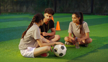 Indian asian young adult gen z woman lady talk casual gossip with fit man coach guy take day break time happy male sitting on ground area place speak give game advice to sports female girl player