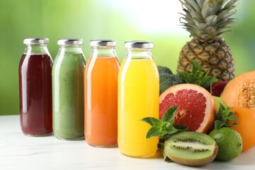 Tasty juices in glass bottles, fresh ingredients and mint on white marble table against blurred green background, closeup
