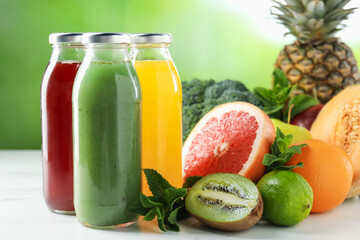 Tasty juices in glass bottles, fresh ingredients and mint on white table against blurred green background, closeup
