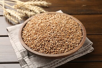 Wheat grains in bowl and spikelets on wooden table, closeup