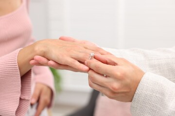 Making marriage proposal. Man putting engagement ring onto his girlfriend's finger at home, closeup