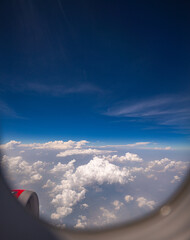 View from airplane window scattered white clouds floating above a vast landscape, with winding...
