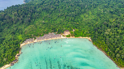 Aerial view of Morgan Village hidden in natural beauty on Surin island Phang Nga. small huts along the coastline, surrounded by lush green jungle. fishing boats are anchored in the turquoise waters. © Narong Niemhom