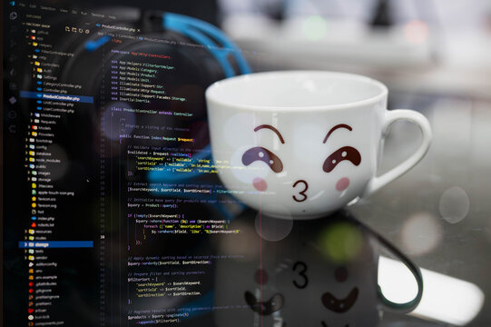 Cute coffee mug with smiling face placed on a desk beside computer screen displaying source code. Perfect for web developers, coders, programmers, tech blogs, and software development content.