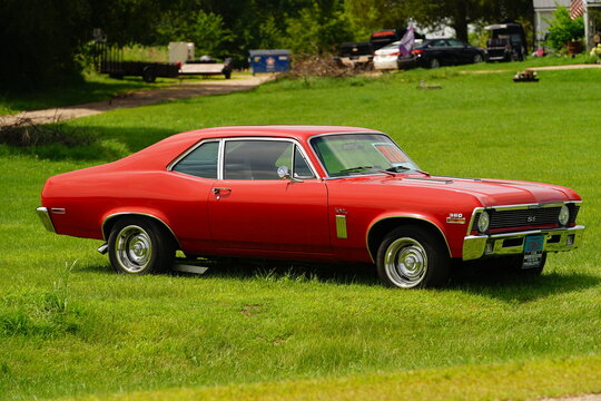 Classic red Chevrolet Nova SS muscle car parked on a lush green lawn, representing vintage American automotive culture and 1970s style.