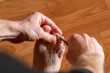 A man gives himself a pedicure, trimming his toenails. A man gives himself a pedicure, using manicure scissors to trim the nails on his feet