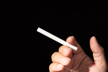 A detailed close-up of a single, unlit white cigarette held in someone's fingers against a soft