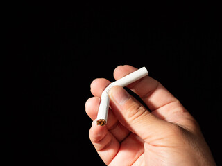 A single hand holds a bent and broken cigarette against a dark background, symbolizing the act of quitting smoking.