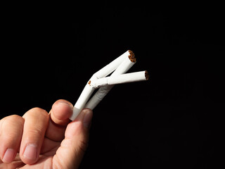 A hand holds several broken cigarettes against a dark background, symbolizing quitting or anti-smoking.