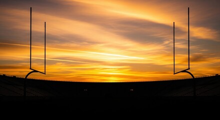 Dramatic silhouette of American football goalposts against a vibrant, fiery sunset sky in a large stadium, evoking the spirit of competition and athletic achievement.