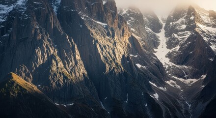 Majestic sunlit mountains with snow-capped peaks amidst misty atmosphere