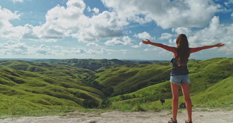 Female tourist standing with open arms, embracing the stunning landscape of rolling green hills and...