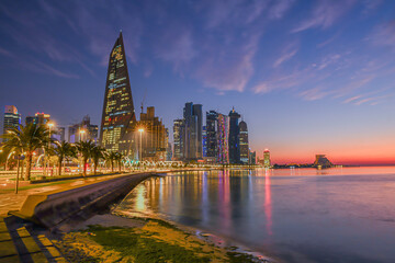 Doha city business downtown center panorama illuminated at sunrise, with modern skyscrapers and sea in the foreground, Qatar