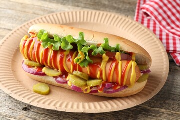 Tasty hot dog with vegetables, mustard and ketchup on wooden table, closeup