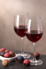 Delicious truffle bonbons and wine on black table against grey background
