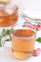 Aromatic tea in glass cup, roses and green leaves on white table, closeup