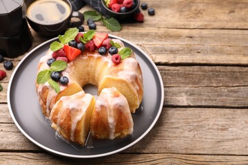 Pieces of delicious bundt cake with berries, glaze and mint on wooden table, closeup