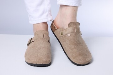 Woman in stylish beige slippers on light floor against grey background, closeup