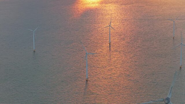 Drone row of offshore wind turbines on shore at sunset, polder, Netherlands