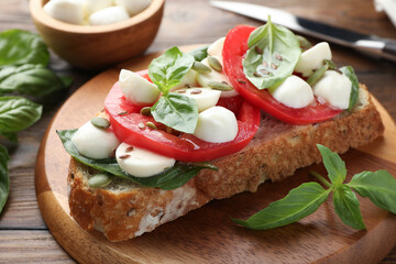 Delicious sandwich with mozzarella cheese, tomatoes and basil on wooden table, closeup