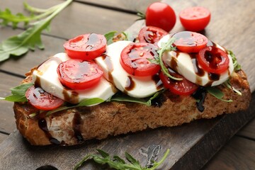 Delicious sandwich with mozzarella cheese, balsamic sauce, tomatoes and arugula on wooden table, closeup