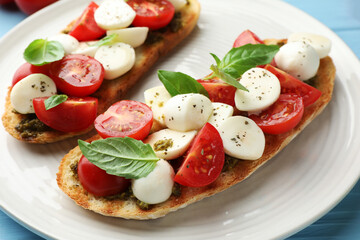 Delicious sandwiches with mozzarella cheese, tomatoes and basil on light blue wooden table, closeup