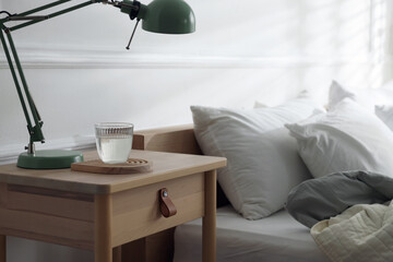Bedside table with lamp and glass of water near bed indoors