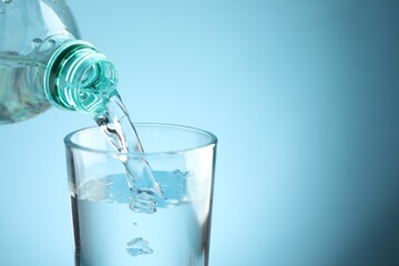 Pouring refreshing soda water from bottle into glass at table against light blue gradient background, closeup. Space for text
