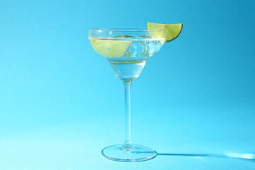 Martini cocktail with slices of lime and mint on light blue background