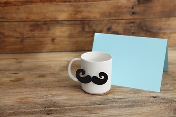 Happy Father's Day. Cup with mustache and card on wooden table. Space for text