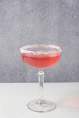 Martini cocktail with sugar in glass on white table near grey wall