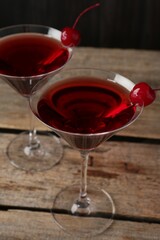 Martini cocktail with cherries in glasses on wooden table, closeup