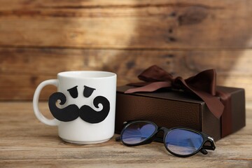 Happy Father's Day. Cup with paper face, gift and glasses on wooden table