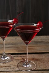 Martini cocktail with cherries in glasses on wooden table, closeup