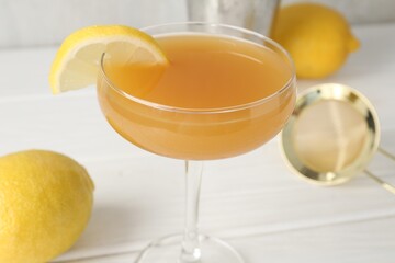 Martini cocktail with lemon slice in glass and fruits on white wooden table, closeup
