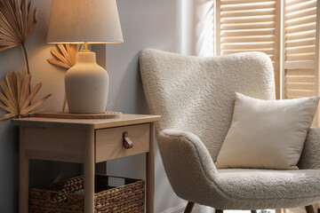 Stylish wooden side table with lamp near armchair at home