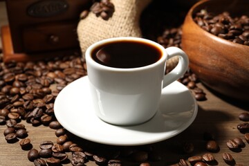 Aromatic coffee in cup and beans on wooden table, closeup