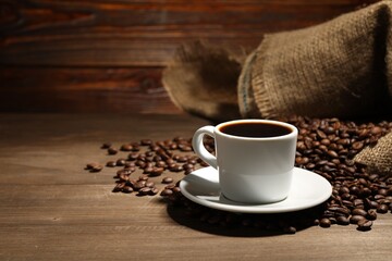 Aromatic coffee in cup and beans on wooden table, space for text