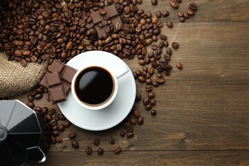 Aromatic coffee in cup, beans, chocolate and moka pot on wooden table, flat lay. Space for text