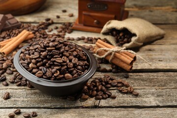Aromatic coffee beans in bowl and cinnamon on wooden table, closeup. Space for text