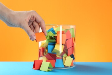 Woman taking orange paper piece from glass jar on color background, closeup
