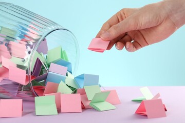 Woman taking pink paper piece from glass jar on color background, closeup
